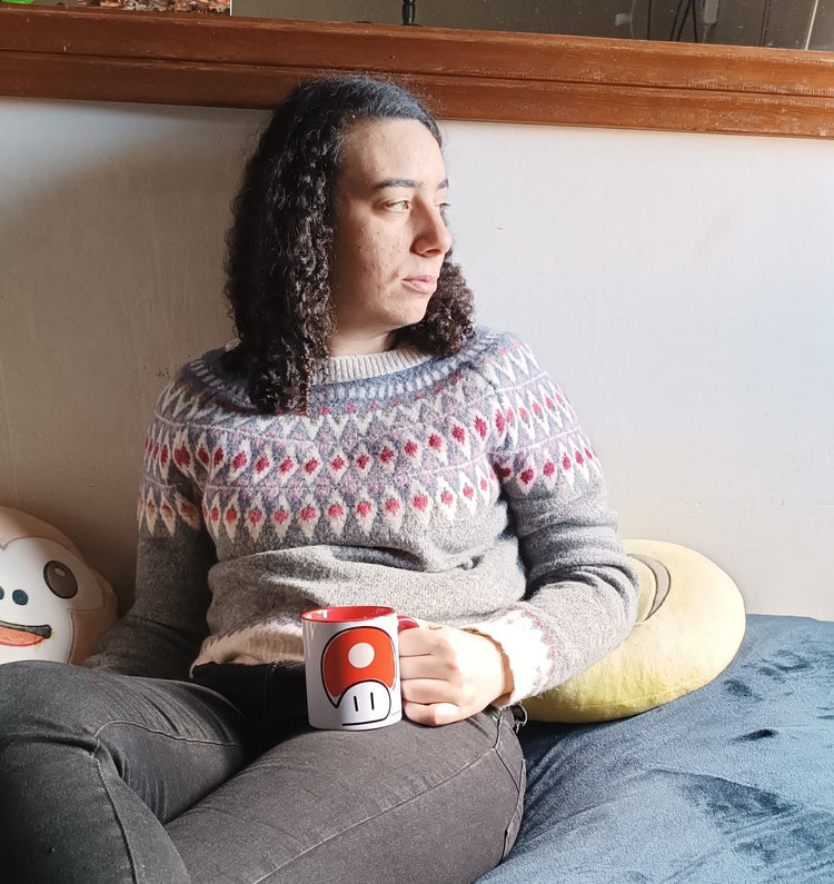 Artesana de ServiArte mirando por la ventana mientras sostiene una taza artesanal en la mano